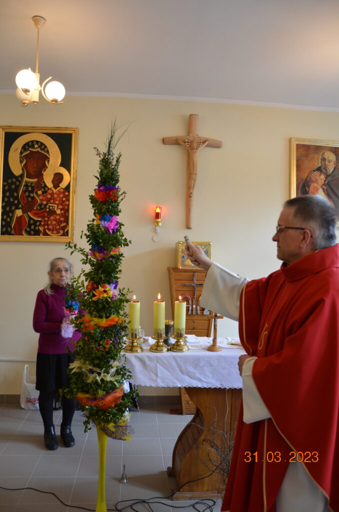 kaplica . Ksiądz Andrzej święci dużą kolorową palnę wykonaną przez nasze panie na terapii zajęciowej