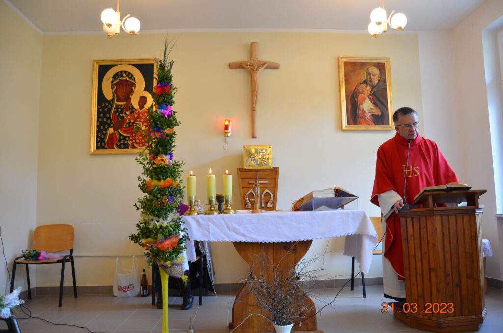 Ołtarz główny. Ksiądz  Andrzej przemawia kazanie. Na ołtarzu głównym wielka kolorowa palma wielkanocna. 