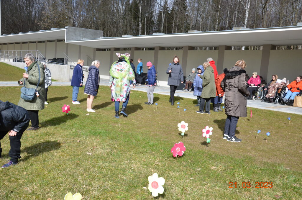 na dworze. spora grupa pań z panią wiosną poszukuje kwiatów na trawie.