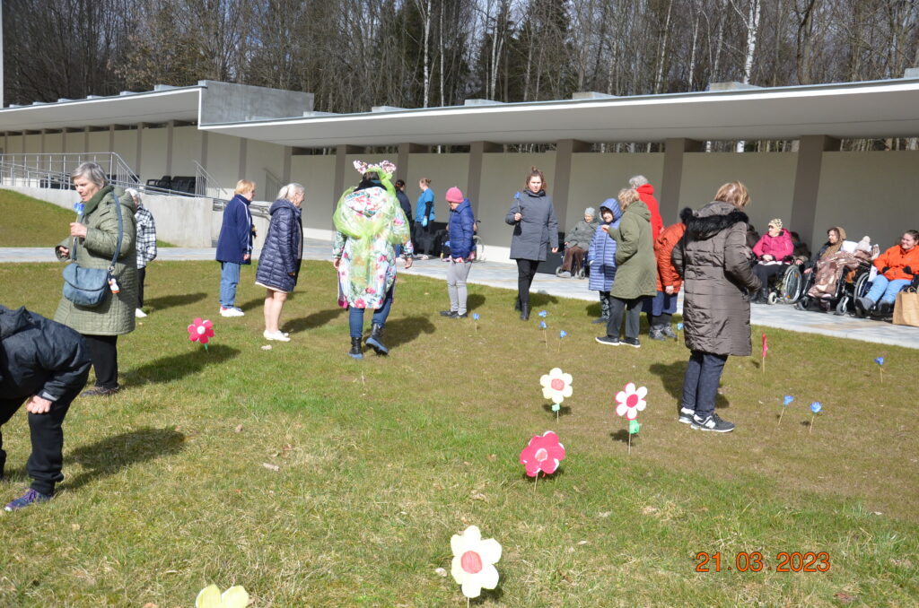 na dworze. spora grupa pań z panią wiosną poszukuje kwiatów na trawie. 