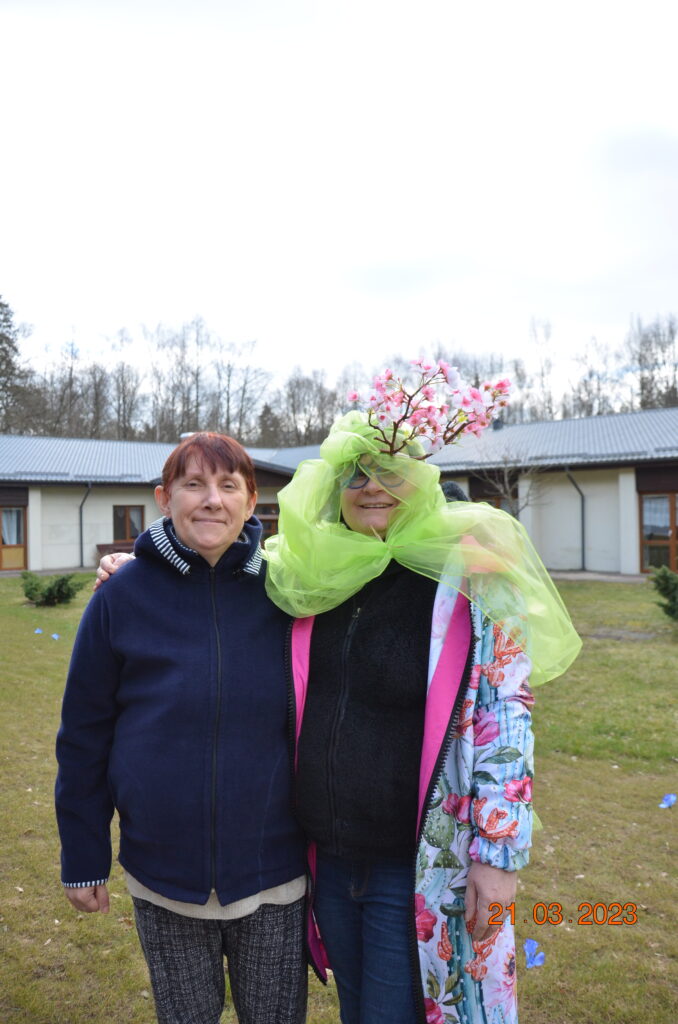 Pani Honorata pozuje do zdjęcia z Panią wiosną , ubrana w kolor zielony, na głowie z kwiatem.