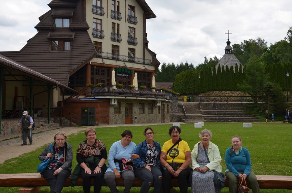 grupa 7 pań siedzi na ławce odpoczywa , w tle park i piękny budynek restauracji w Szymbarku
