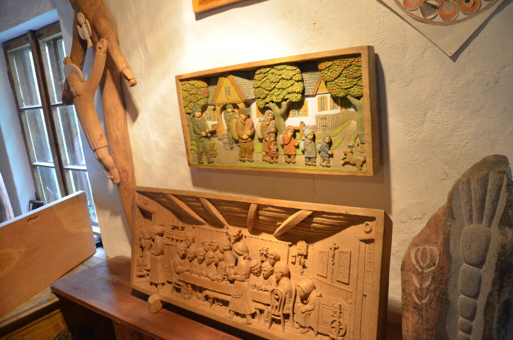 w środku skansenu.  zdjęcie przedstawia dwie płaskorzeźby oraz drewniany krzyż z Chrystusem. 