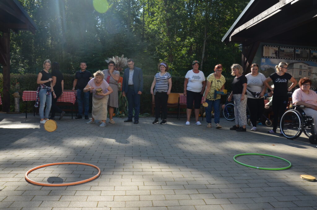 słoneczny dzień, zawody sportowe, dwa okręgi leża na ziemi, dwóch zawodników wrzuca do celu krążki z drewna, z boku grupa kilku osób dopinguje 