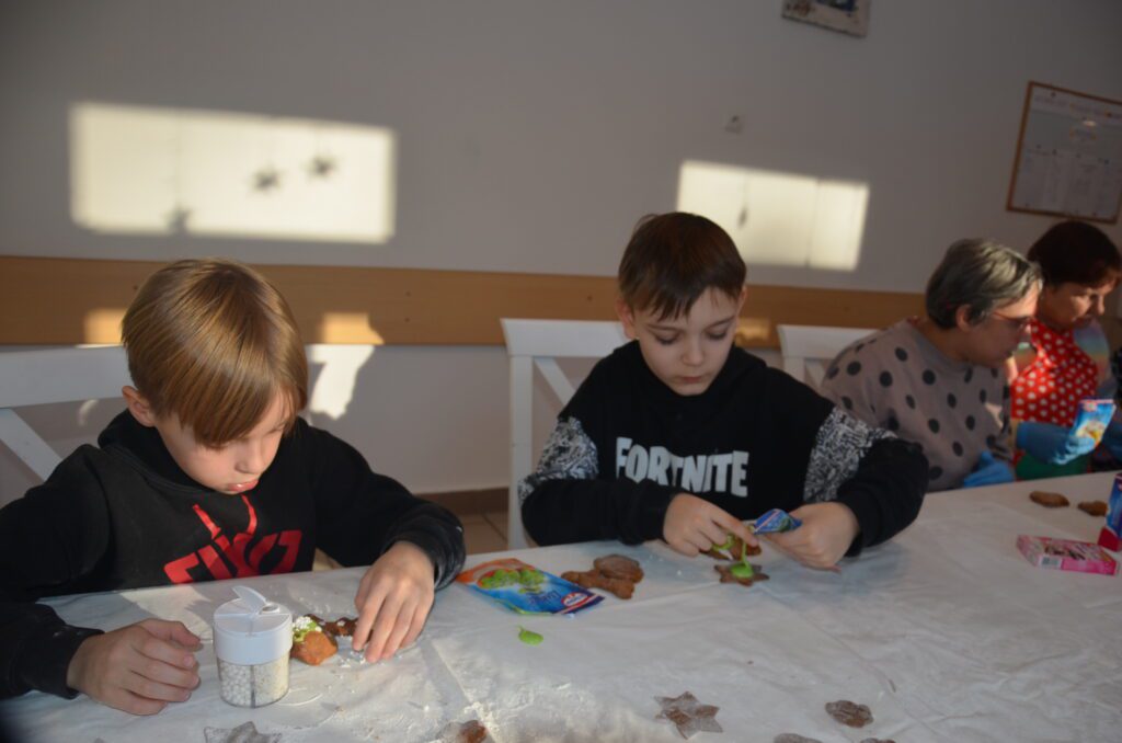na stołówce. dwóch chłopców dekoruje upieczone ciasteczka piernikowe