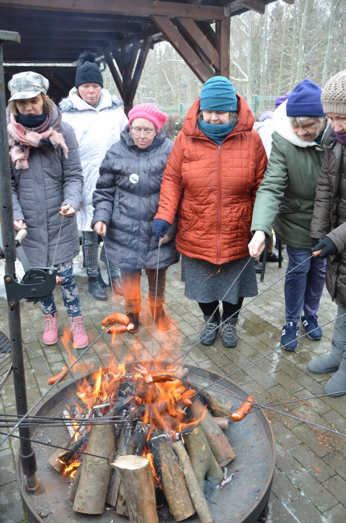 na dworze. grupa pięciu pań stoi przed ogniskiem, piecze kiełbaski na kiju