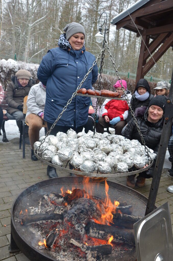 Przy ognisku. zimowa aura, grupa mieszanek siedzi wokół ogniska, piecze się na ogniu zawinięte w folię ziemniaki i kiełbaski 