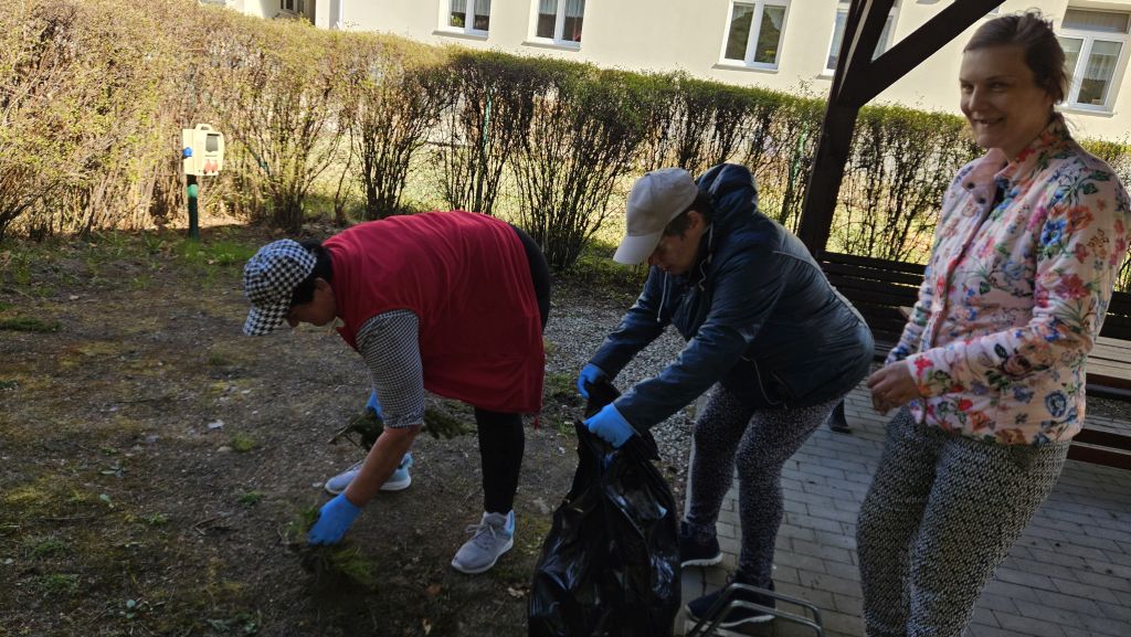 inne miejsce pod wiatami, 3 kobiety, 1 jest  schylona- coś wyrywa, jedna trzen=ma worek, a trzecia sie uśmiecha do aparatu
