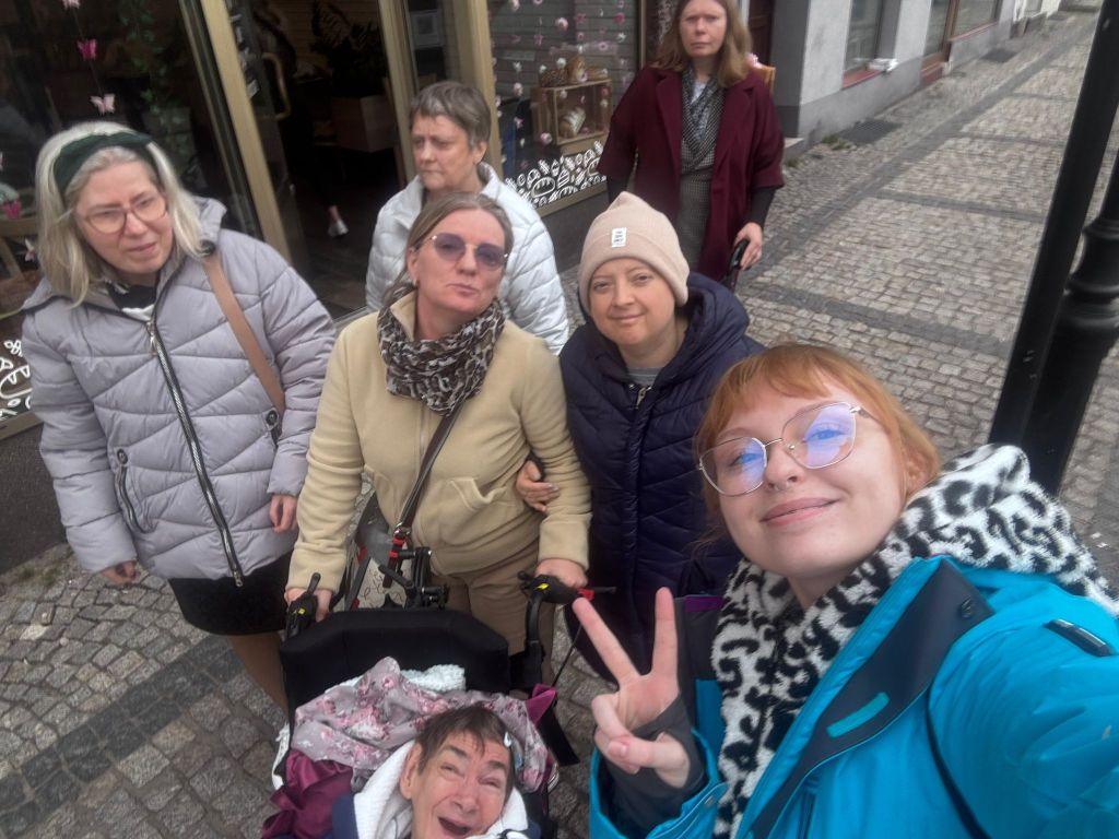 uliczka , te same panie uśmiechnięte  pozują do zdjęcia , widać witrynę jakiegoś sklepu