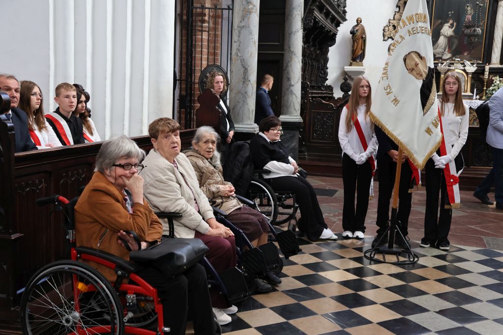 katedra wnętrze 4 panie z naszego domu siedzą na ławkach, widoczny jest sztandar  księdzem  trzymany przez młodzież