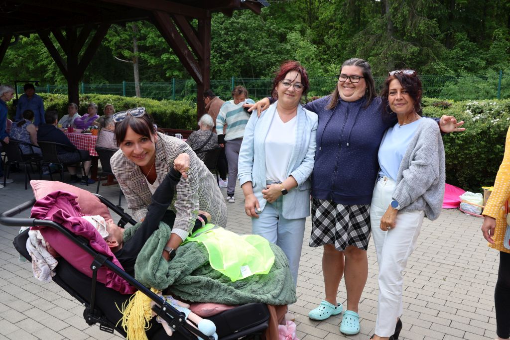 na przedzie 4 kobiety pozója do zdjęcia i jedna kobieta jest na wózku, w tle widać inne osoby siedzace przy stole w obrusy w czerwoną kratę
