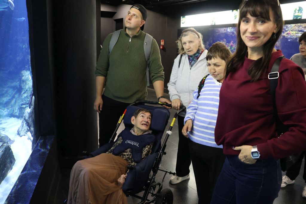 grupę ludzi stojącą przy scianie akwarium jedna pani jest na wózku